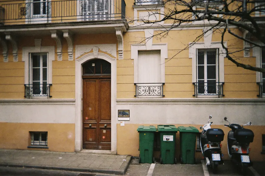 Façade d'immeuble Belle Époque avec bacs à ordures et scooters
